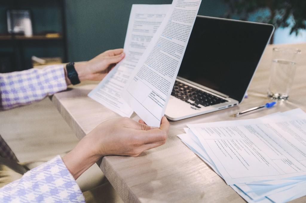 Expert reviewing printed country conditions documents at a desk with laptop and research materials